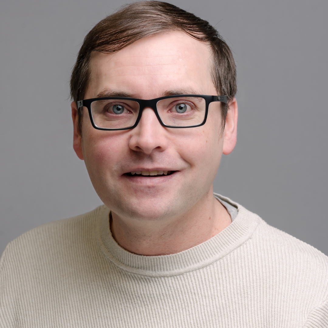 Image of a male smiling wearing a grey suit.