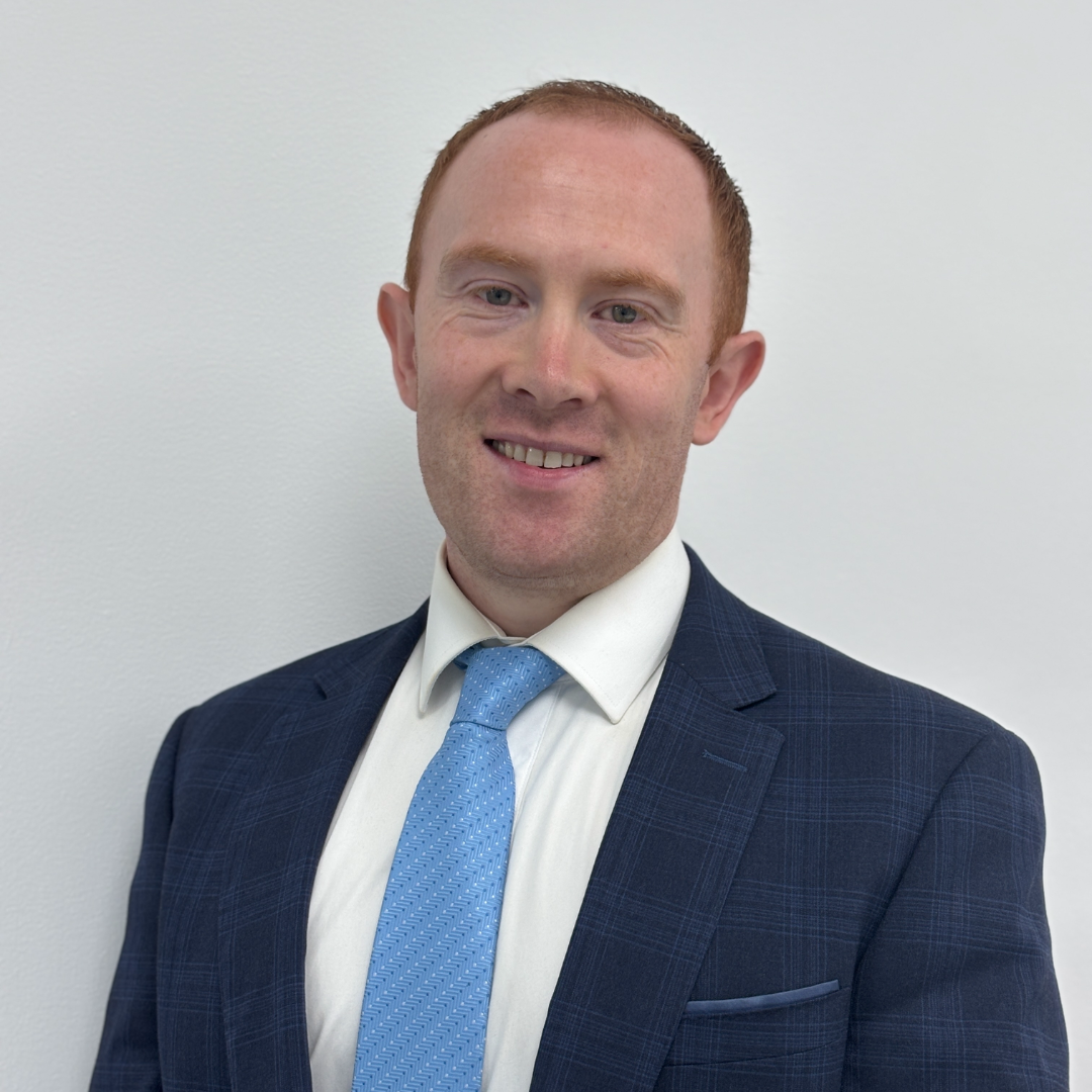 Image of a male smiling wearing a grey suit.