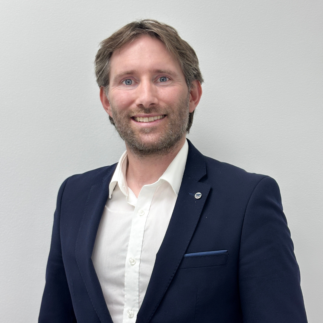 Image of a man smiling wearing a navy suit. 
